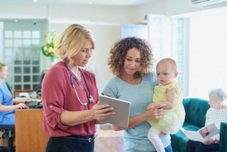 Doctor showing patient with baby something on a tablet in hospital reception