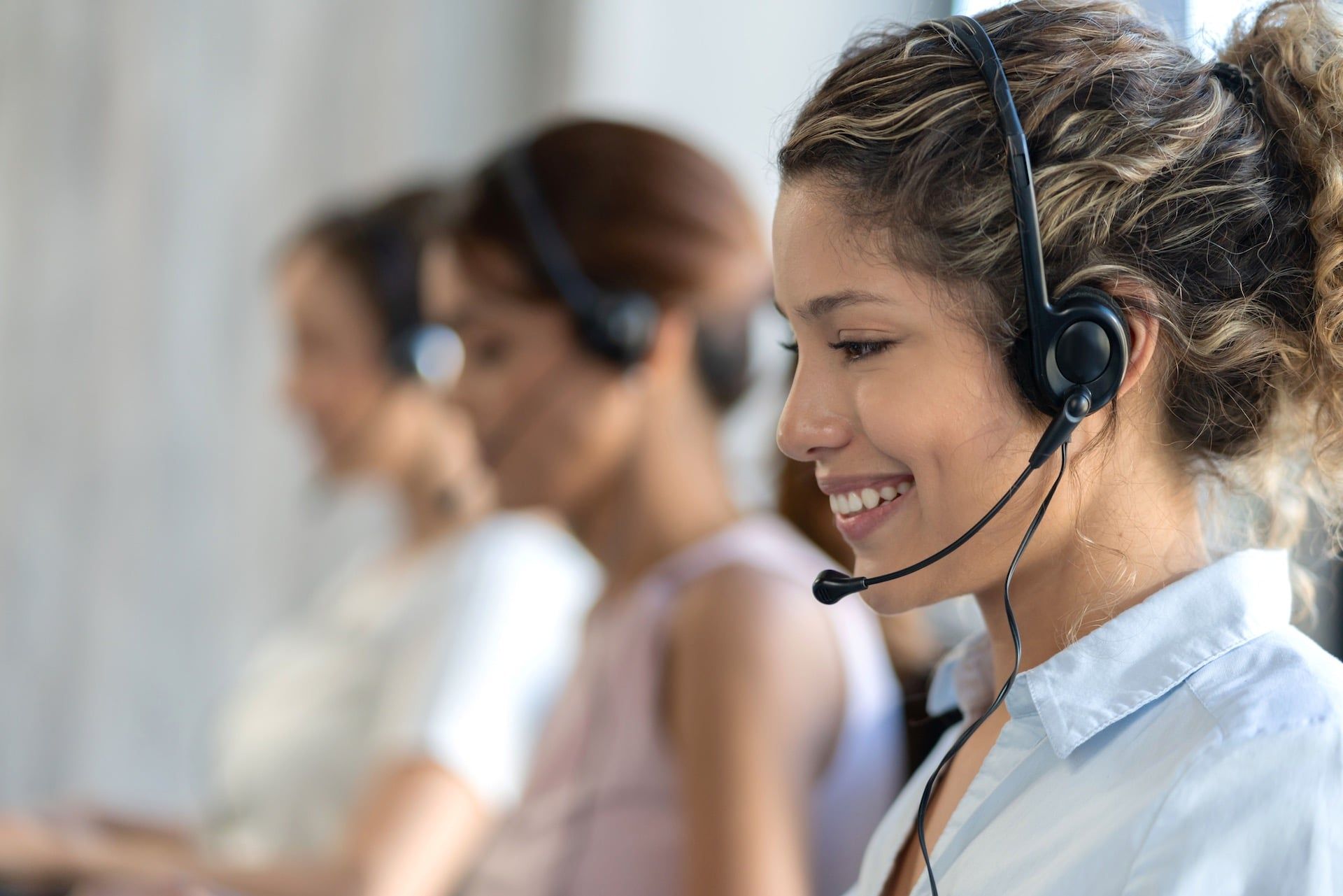 Smiling girl with curly hair answering calls in healthcare verticals environment with hospital clothes and headset - Behavioral Health Business Process Outsourcing