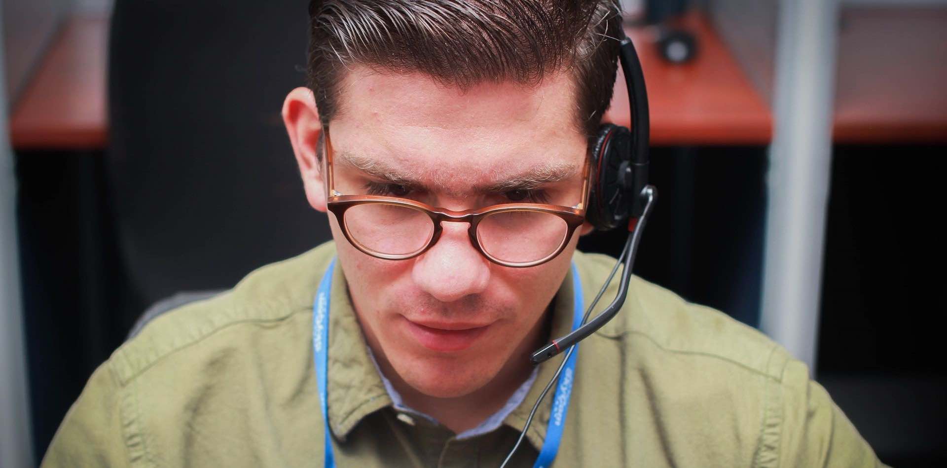 Male agent with glasses, green shirt and headset looking down while working