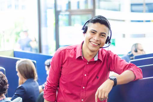 Male Call Center agent with red shirt standing in room with other agents