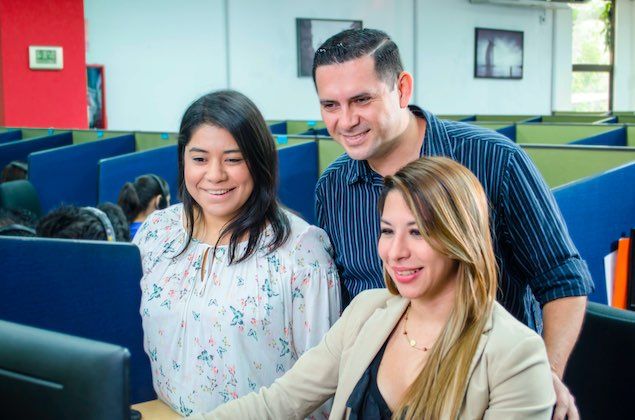 Call center manager showing two agents something on a screen in the office