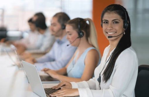 BPO female agent sitting by desk smiling with colleagues