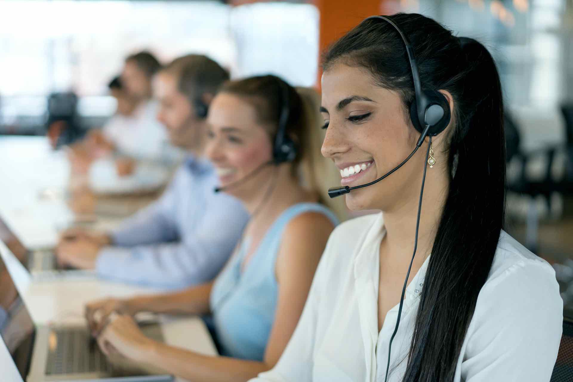 Woman smiling while wearing headset next to call center agents in office
